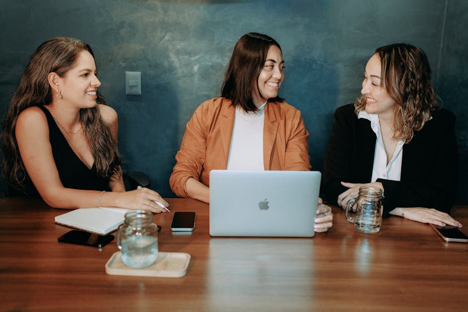 Three women in a professional setting, collaborating over a laptop in an office.